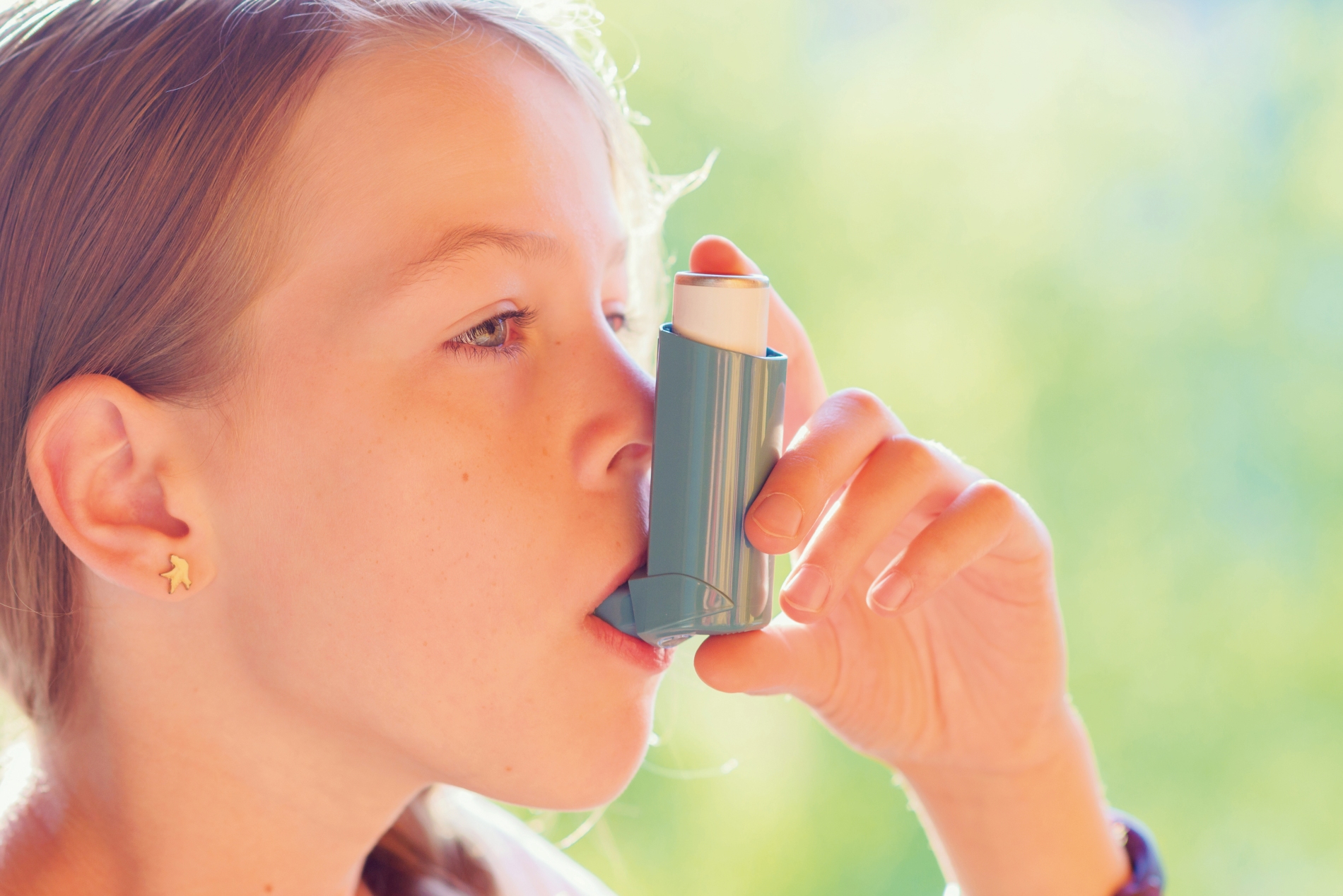 Kind hält einen Asthma-Inhalator, Nahaufnahme einer Hand mit Inhalator vor grünem Hintergrund.