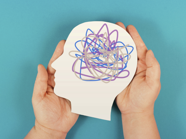 Illustration eines menschlichen Kopfes mit farbigem Gedankenchaos, gehalten von zwei Händen, symbolisiert mentale Gesundheit.